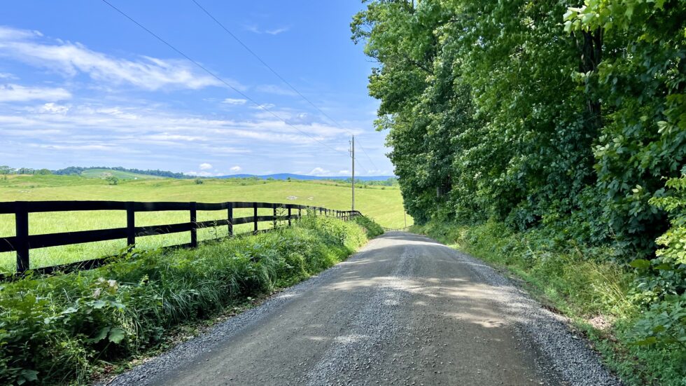 a dirt road with a fence and grass field